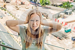 A young woman by the window annoyed by the building works outside. Noise concept