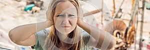 A young woman by the window annoyed by the building works outside. Noise concept BANNER, long format