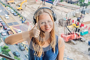 A young woman by the window annoyed by the building works outside, wired soundproof wireless headphones. Soundproofing