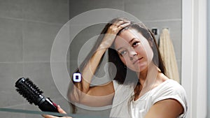 Young woman winds curls on a brush attachment using a multi-styler hairdryer at home bathroom. The concept of hair care