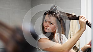 Young woman winds curls on a brush attachment using a multi-styler hairdryer at home bathroom. The concept of hair care