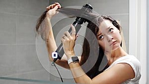 Young woman winds curls on a brush attachment using a multi-styler hairdryer at home bathroom. The concept of hair care