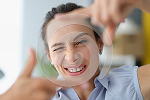 Young woman winks and makes a gesture with hands to photo frame