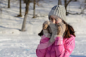 Young woman in winter clothes in the background of the forest. Brunette in pink down jacket, knitted hat, scarf and gloves on a wi