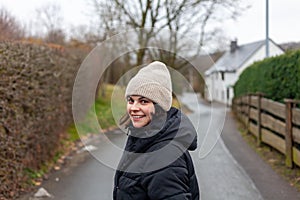 Young woman in a winter jacket and knitted hat walking on a country lane