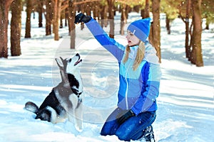 Young woman in winter snowy forest walking with her dog in a winter day. Friendship pet and human.