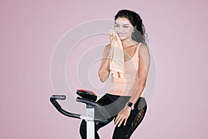 Young woman wipes her sweat on an exercise bike