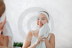 Young woman wipes herself face with white towel after shower washing. Self care in morning at bathroom. Happy smiling