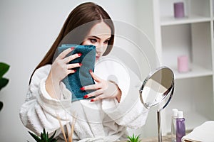 Young woman wiping her face with towel in bathroom.