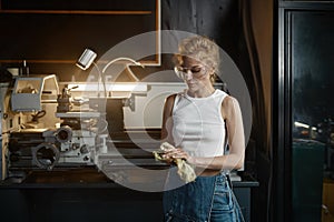 Young woman wiping her hands with rag after working on lathe turning machine