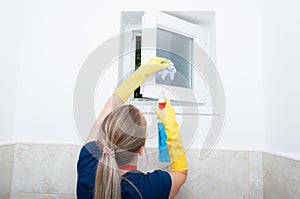 Young woman wiping small window at home