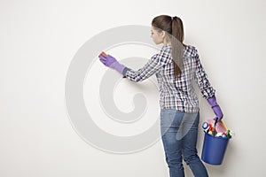 Young woman wiping white wall from dust