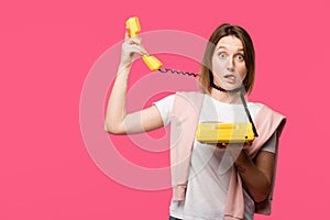 young woman with wire around neck holding rotary phone and looking at camera isolated