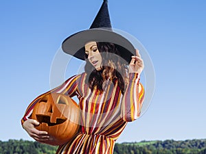 Young woman with witch hat holding pumpkin outdoors