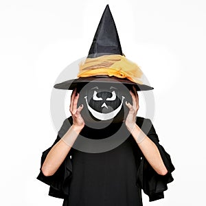 Young woman in witches hat and costume holding pumpkin in front of her face. Halloween Witch with scary face Jack o Lantern.