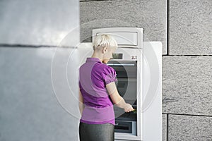 Young woman withdrawing money with card at atm