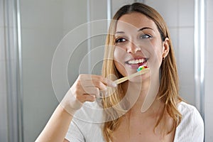 Young woman with wooden bamboo tooth brush in the bathroom looking herself in the mirror. Dental care, eco-friendly bamboo