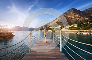 Young woman on wooden pier on sea shore is looking on mountain