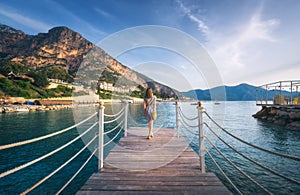 Young woman on wooden pier on sea shore is looking on mountain