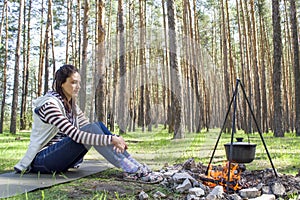 Young woman in the woods near the fire with a pot