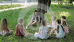 Young woman at work as educator reading book to boys and girls in park