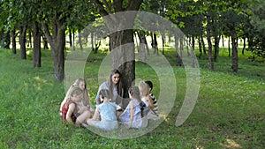 Young woman at work as educator reading book to boys and girls in park