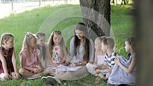 Young woman at work as educator reading book to boys and girls in park