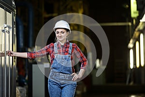 Young woman in a work dress and white hard hat in a factory. Woman in a work uniform. Working process.