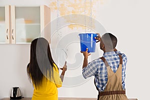 Young Woman And Worker Collecting Water In Bucket From Ceiling