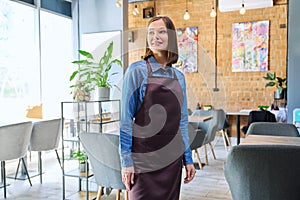Young woman worker, owner in apron looking at camera in restaurant, coffee shop