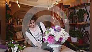 Young woman working as florist in flower shop and looking at camera, smiling with bouquet on desk