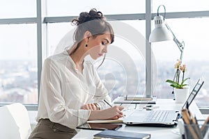Young woman working as an office manager, planning work tasks, writing down her schedule to planner at the workplace. photo
