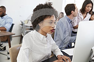 Young woman working at computer in a busy open plan office