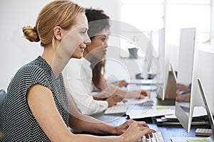 Young woman working at computer in office beside colleagues