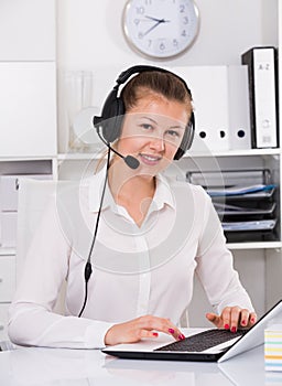 Young woman is working at a computer and talking by headset with client