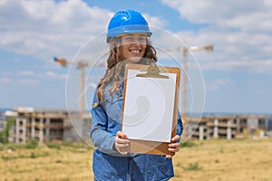 young woman working in construction site and holding clipboard with documents