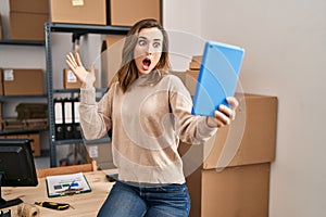 Young woman working ecommerce doing video with tablet scared and amazed with open mouth for surprise, disbelief face