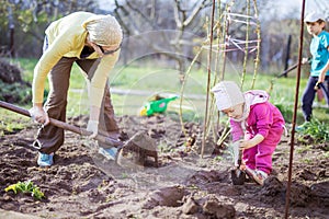 Young woman working in garden while her daughter and son playing beside her