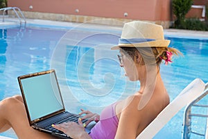 Young woman working on his laptop by the pool while on vacation