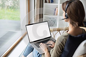Young woman working at home. Student girl wearing headset using laptop computer with empty white blank screen.