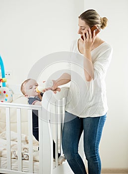 Young woman working at home and talking by phone while feeding h