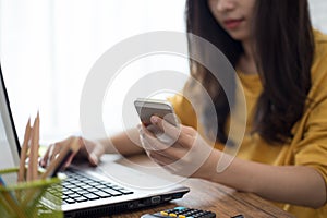 young woman working from home using smart phone and notebook computer