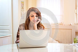 Young woman working with laptop computer at home, serious, thinking.