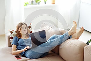 Young woman working with laptop computer lying on sofa at home. Freelancer or blogger. Distance learning of new profession.