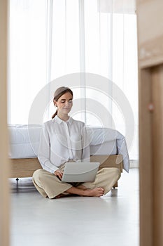 Young woman working on laptop computer while sitting on floor at the bedroom.
