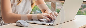 Young woman is working on a laptop on her balcony overlooking the skyscrapers. Freelancer, remote work, work from home BANNER, lon
