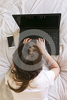 Young woman working on laptop at home on bed. View from above