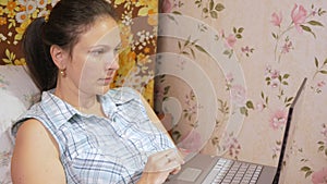 Young woman working on laptop at home on couch. Attentively presses on the touchpad