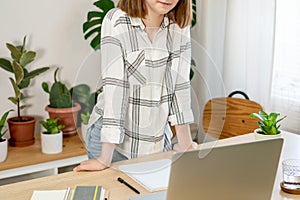 Young woman working on laptop at home. Cozy home office workplace, remote work, e-learning concept.