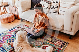 young woman working on laptop at home. cute golden retriever dog besides. healthy breakfast time. technology and lifestyle indoors